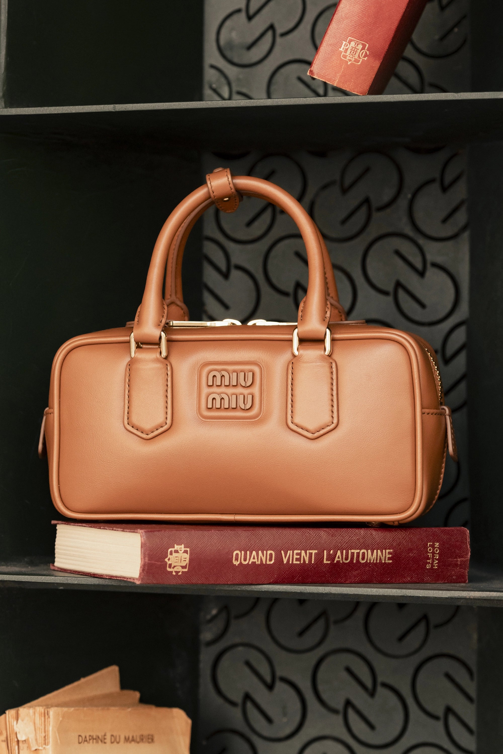 Sac Miu Miu camel posé sur des livres anciens, illustrant la tendance des accessoires minimalistes et intemporels à adopter cette saison dans le guide des 10 tendances mode.