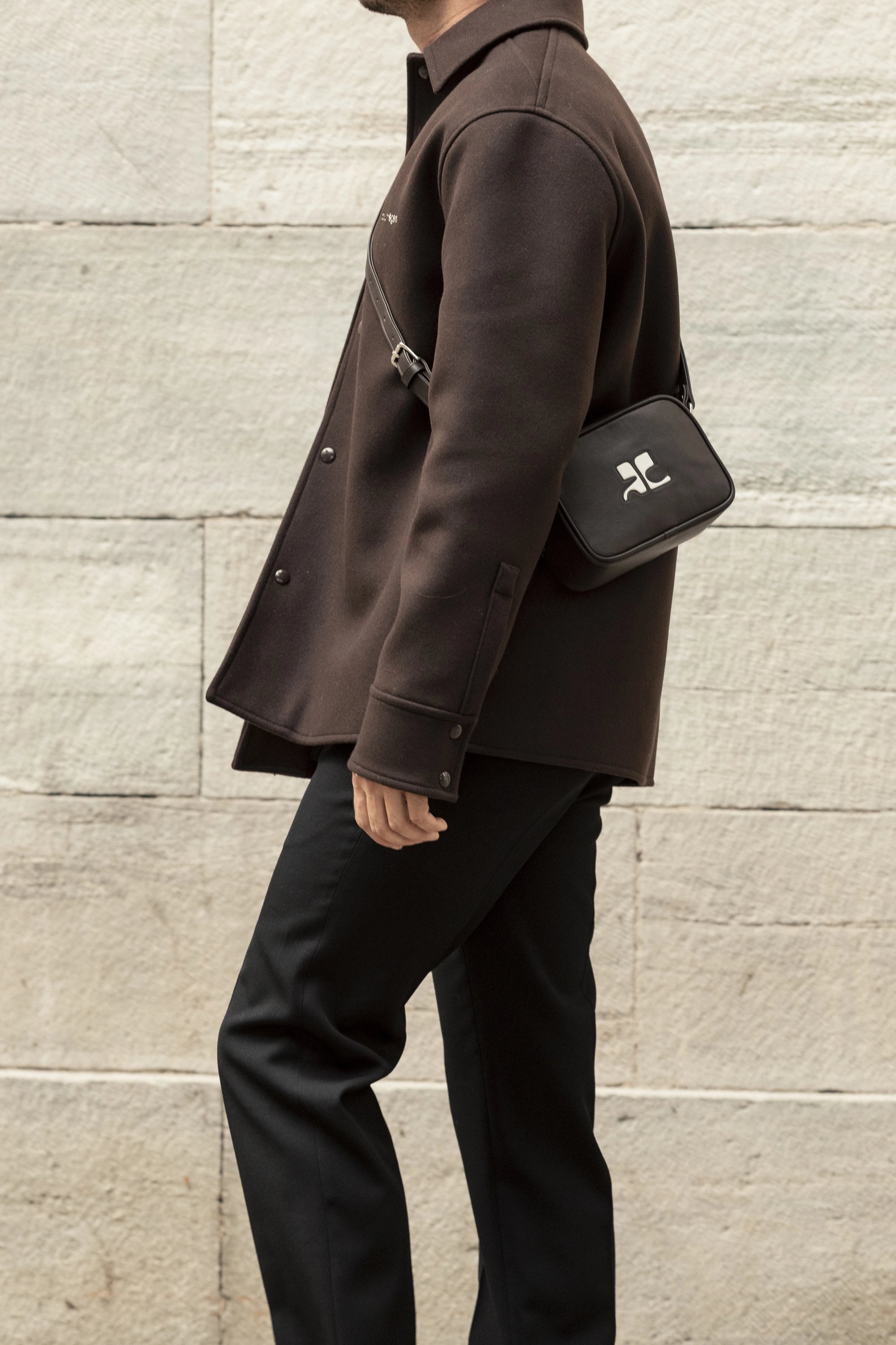 Look masculin contemporain avec veste marron et sac bandoulière noir, illustrant la tendance streetwear chic et les accessoires minimalistes de la saison.